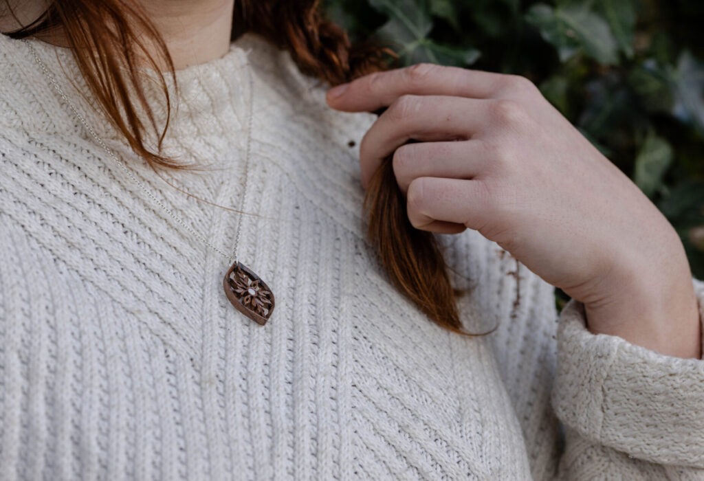 Bijou délicat en bois sculpté en noyer et nacre, porté par une femme vêtue d'un pull blanc